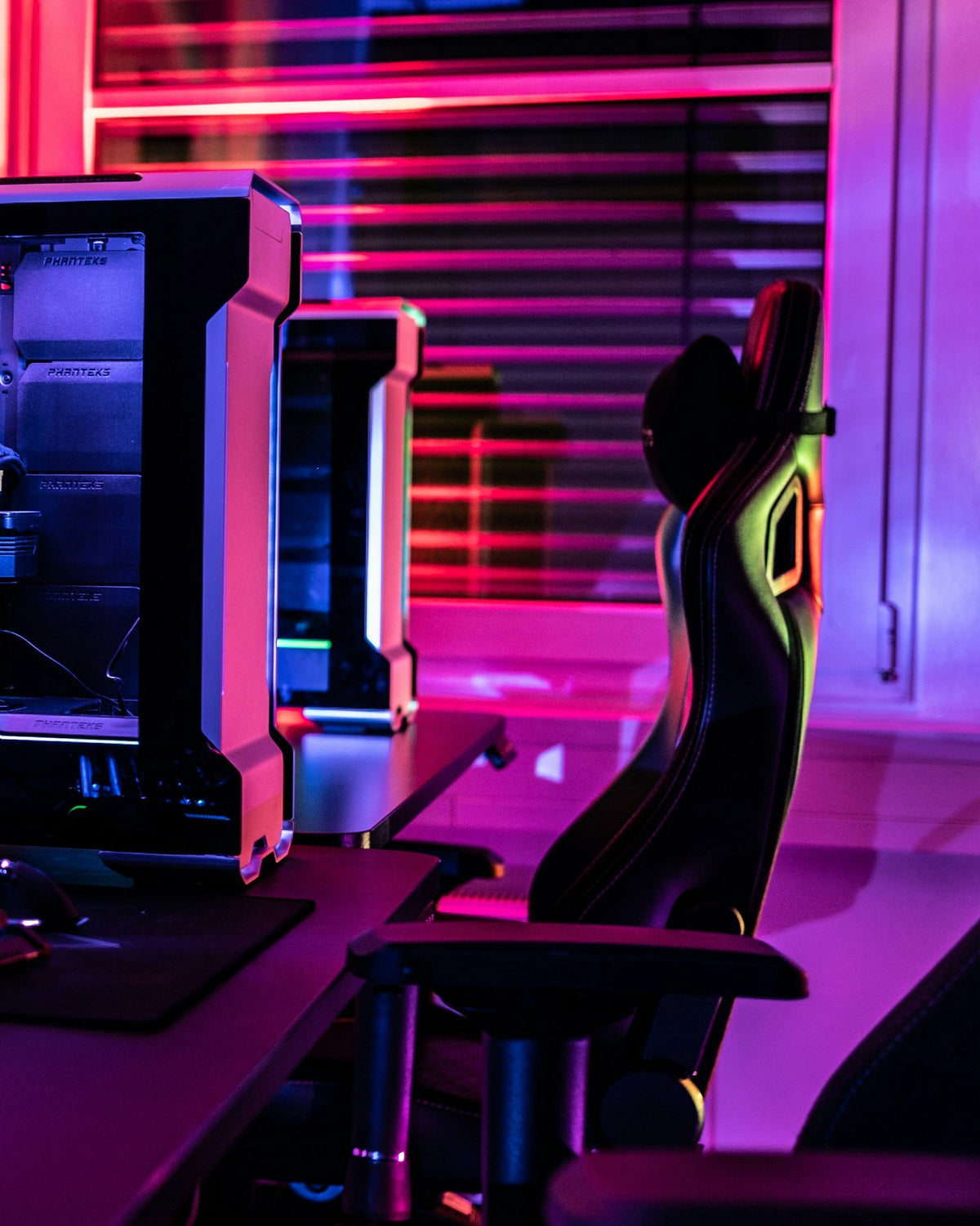 Gaming desk with a monitor, a lit PC and a gaming chair under pink and violet light