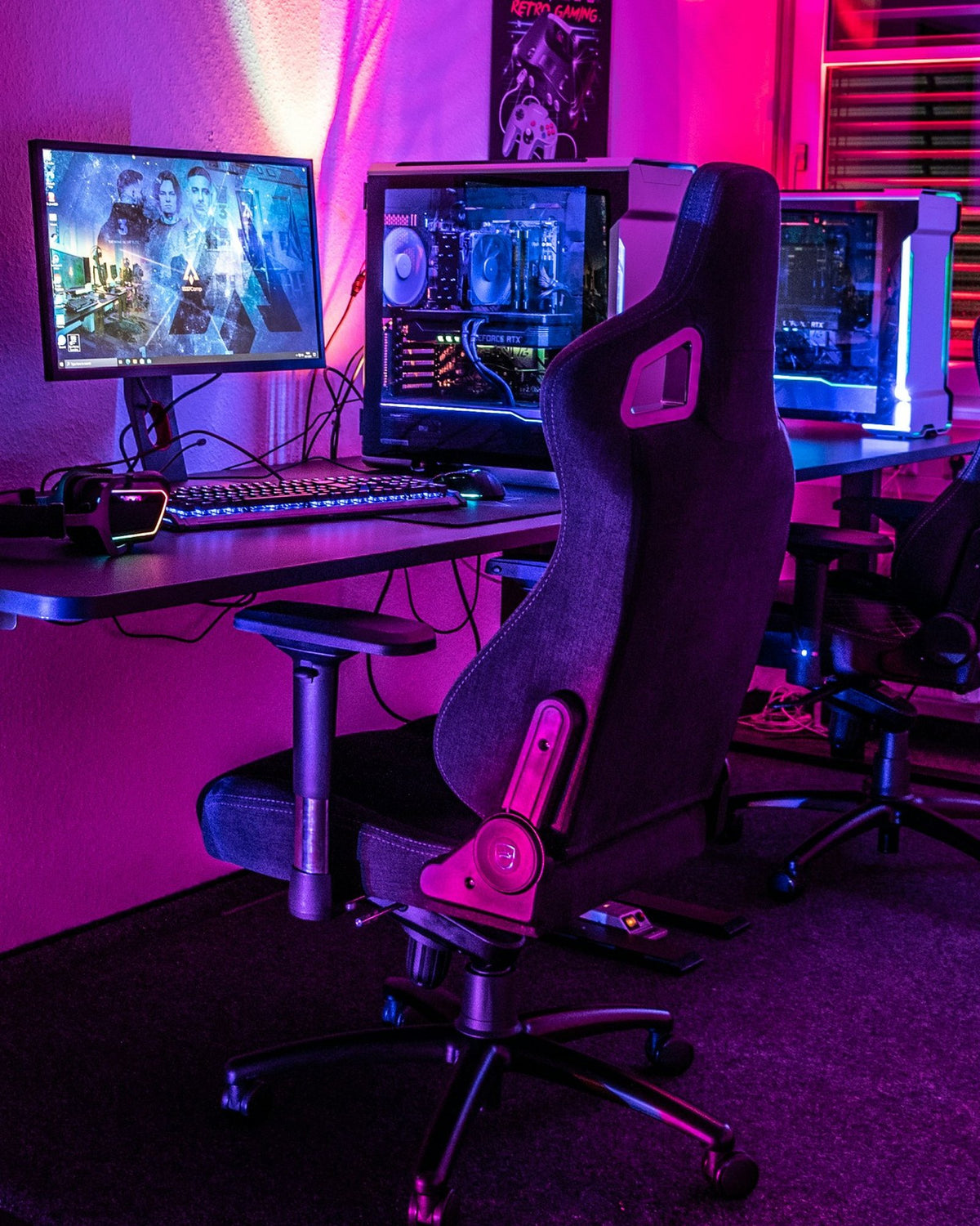 Gaming room with two gaming chairs at a long desk under pink light