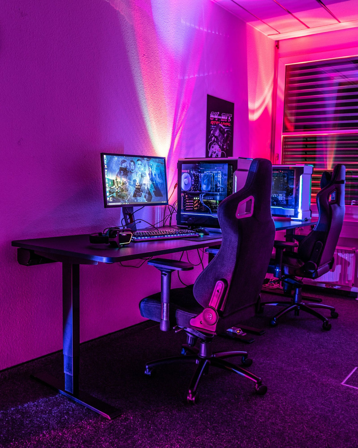 Gaming room with two gaming chairs at a long desk under pink light